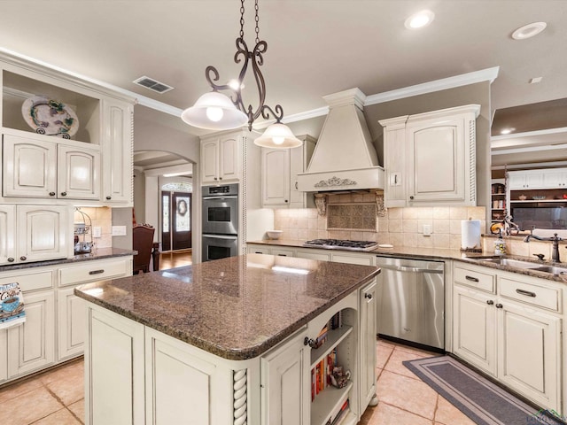 kitchen with premium range hood, stainless steel appliances, sink, a kitchen island, and hanging light fixtures