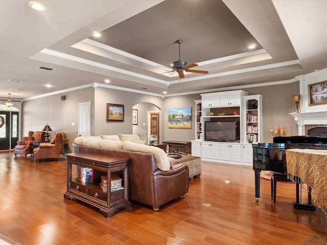 living room with ceiling fan, light wood-type flooring, ornamental molding, and a tray ceiling