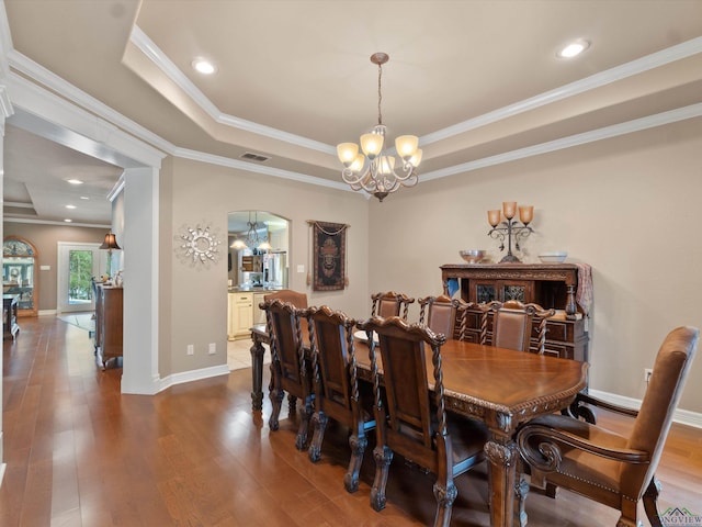 dining area with a tray ceiling, an inviting chandelier, wood-type flooring, and ornamental molding