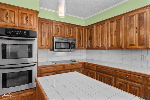 kitchen with decorative backsplash, a textured ceiling, stainless steel appliances, and tile counters