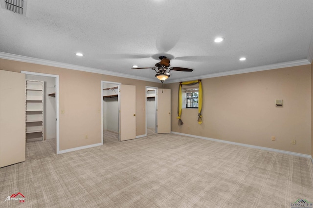 unfurnished bedroom featuring crown molding, ceiling fan, a spacious closet, a textured ceiling, and light colored carpet