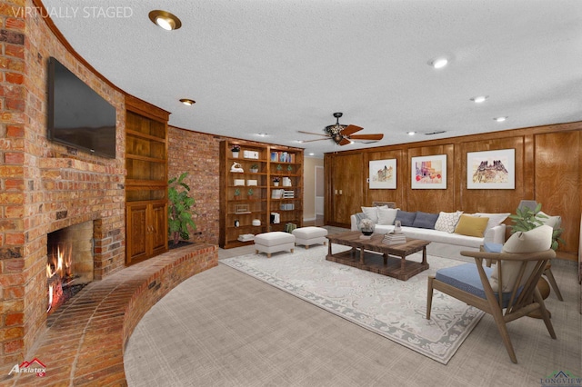 living room featuring ceiling fan, built in features, a textured ceiling, wooden walls, and a fireplace