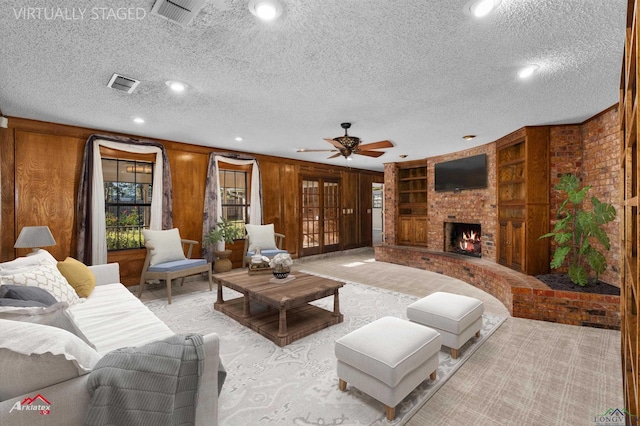 living room featuring wood walls, a brick fireplace, ceiling fan, built in features, and a textured ceiling