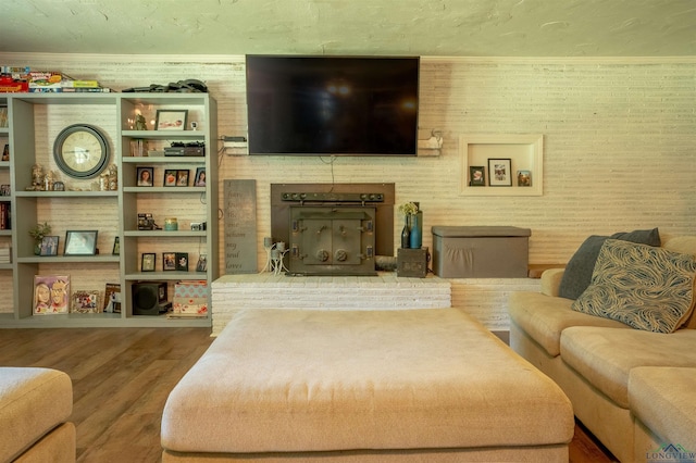 living room featuring hardwood / wood-style flooring, brick wall, and ornamental molding