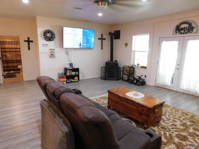 living room featuring a wood stove, ceiling fan, french doors, and light wood-type flooring