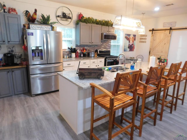 kitchen with a barn door, light stone counters, pendant lighting, a kitchen bar, and appliances with stainless steel finishes