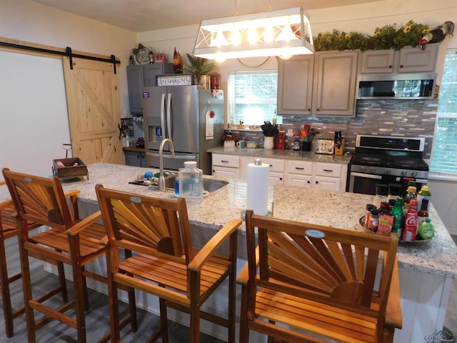 kitchen featuring light stone countertops, tasteful backsplash, stainless steel appliances, a barn door, and decorative light fixtures