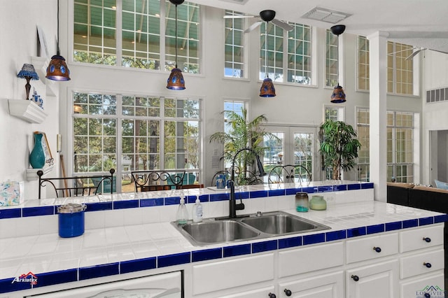 kitchen featuring white cabinetry, tile counters, sink, and a high ceiling