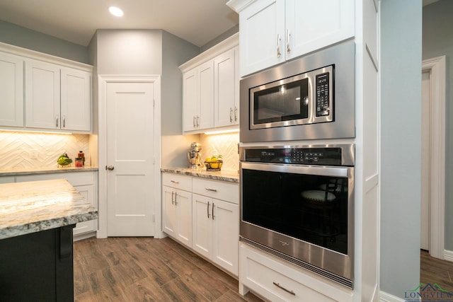 kitchen with backsplash, light stone counters, stainless steel appliances, dark wood-type flooring, and white cabinetry