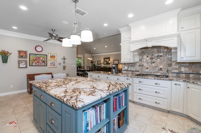 kitchen featuring stainless steel gas stovetop, ceiling fan, light stone countertops, blue cabinetry, and a kitchen island