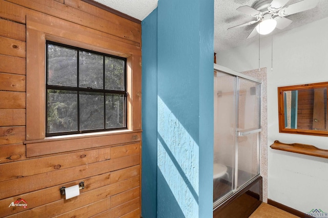 bathroom featuring ceiling fan, wood walls, and a textured ceiling