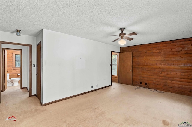 empty room with light carpet, a textured ceiling, ceiling fan, and wooden walls