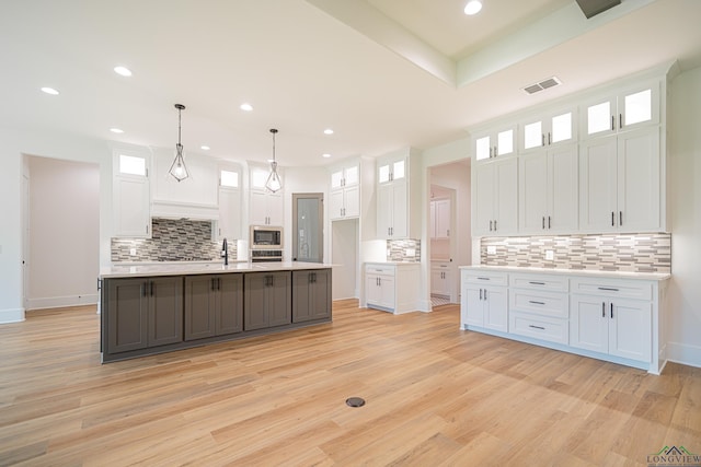 kitchen featuring a kitchen island with sink, built in microwave, decorative light fixtures, light hardwood / wood-style flooring, and white cabinetry