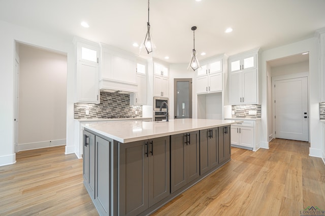 kitchen featuring pendant lighting, white cabinets, a center island with sink, light wood-type flooring, and gas cooktop