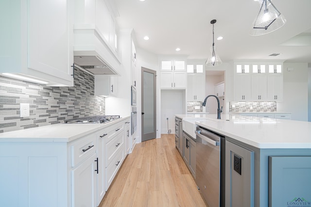 kitchen with white cabinets, a center island with sink, sink, hanging light fixtures, and appliances with stainless steel finishes