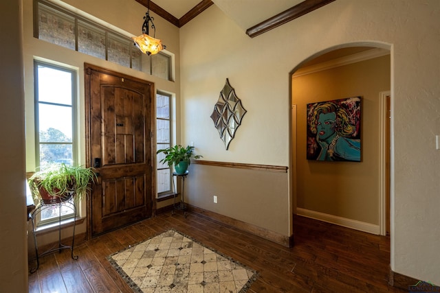 foyer with a healthy amount of sunlight, crown molding, and dark wood-type flooring