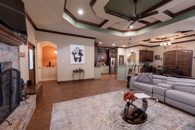 living room featuring crown molding, a fireplace, dark hardwood / wood-style floors, and ceiling fan with notable chandelier