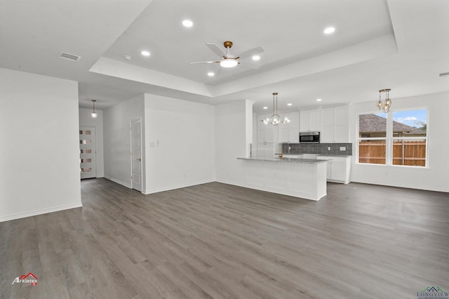 unfurnished living room featuring ceiling fan with notable chandelier, a tray ceiling, and hardwood / wood-style flooring