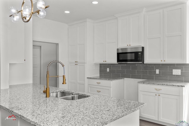 kitchen featuring light stone countertops, backsplash, white cabinetry, and sink