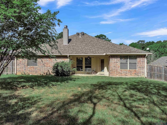 back of property featuring a chimney, brick siding, fence, and a lawn