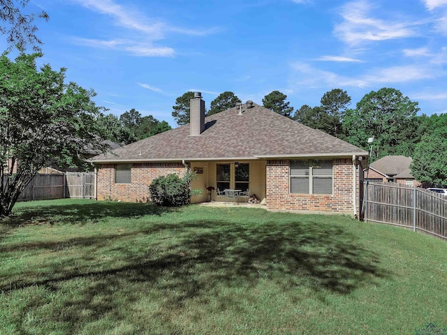 rear view of house featuring a chimney, a shingled roof, a fenced backyard, a lawn, and brick siding