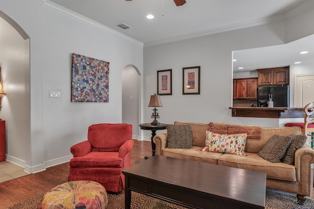 living area featuring arched walkways, wood finished floors, crown molding, and ceiling fan