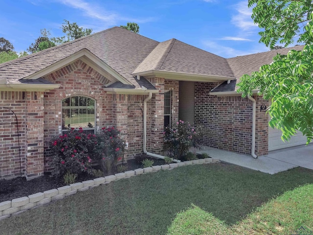 single story home featuring a front lawn, driveway, a shingled roof, a garage, and brick siding