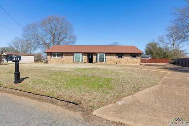 ranch-style home featuring brick siding, roof with shingles, a front yard, and fence