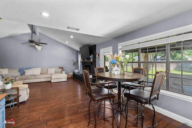 dining space featuring lofted ceiling, dark wood-style floors, a fireplace with raised hearth, ceiling fan, and recessed lighting