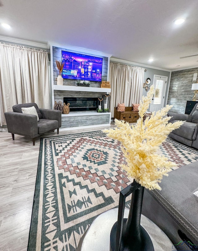 living room with a glass covered fireplace, recessed lighting, wood finished floors, and ornamental molding