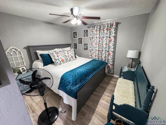 bedroom with ceiling fan, a textured ceiling, wood finished floors, and a textured wall