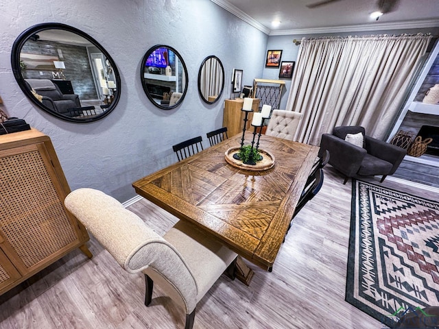 dining area with wood finished floors, a textured wall, baseboards, and ornamental molding