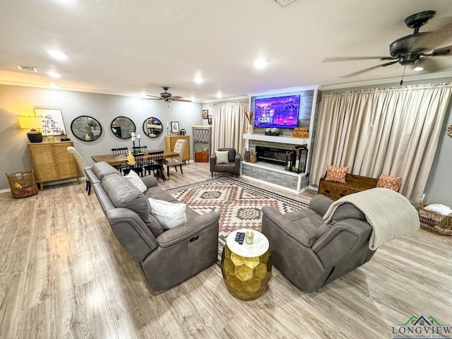 living room with a glass covered fireplace, visible vents, wood finished floors, and a ceiling fan