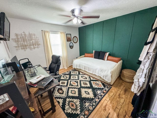 bedroom with a decorative wall, light wood-style floors, ceiling fan, and a textured ceiling