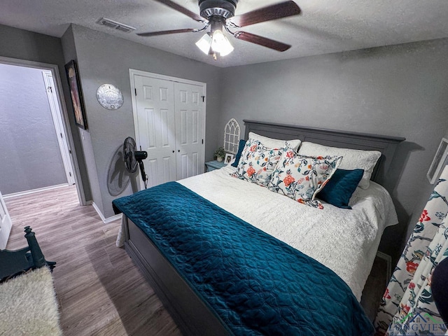 bedroom with a closet, visible vents, a textured ceiling, and wood finished floors