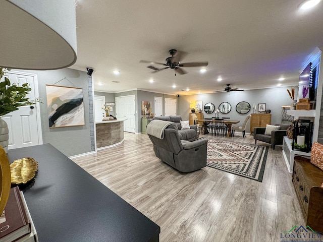 living area with a ceiling fan, light wood-style floors, a fireplace, and ornamental molding