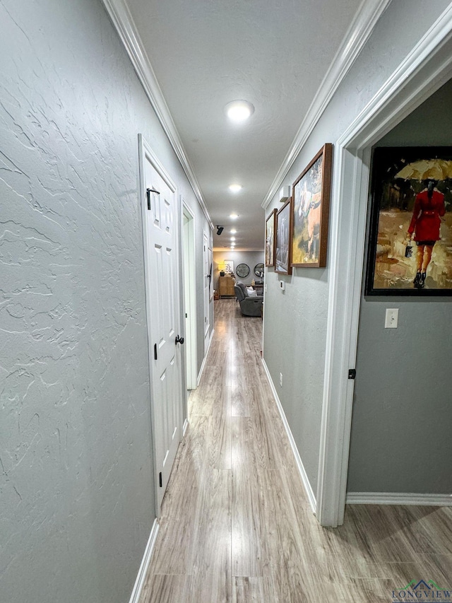 hall with baseboards, crown molding, light wood-style floors, and a textured wall