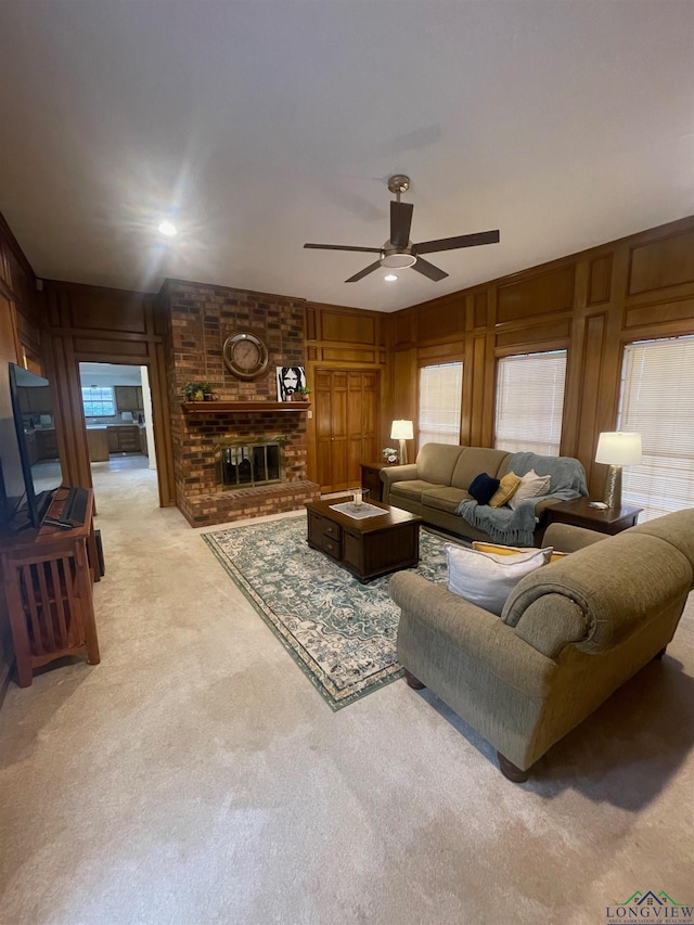 living room with wood walls, light colored carpet, a wealth of natural light, and a brick fireplace