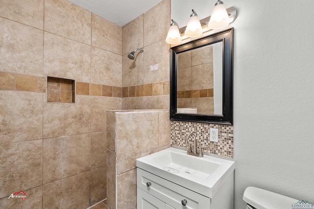 bathroom with vanity, a tile shower, backsplash, and toilet