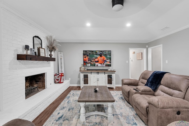 living room with crown molding, wood finished floors, a fireplace, baseboards, and visible vents