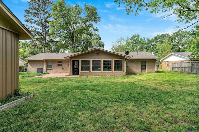 rear view of property featuring a lawn, fence, and brick siding