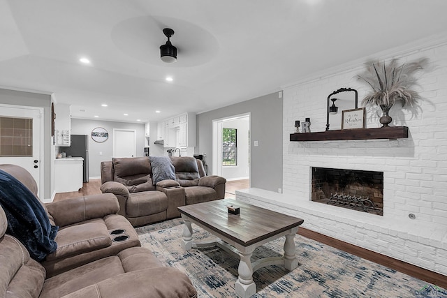 living area featuring a ceiling fan, light wood-style flooring, baseboards, a brick fireplace, and recessed lighting
