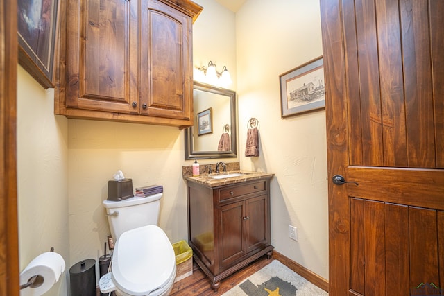 half bath featuring baseboards, vanity, and toilet