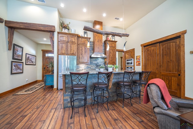 kitchen featuring a breakfast bar area, stainless steel appliances, dark wood-type flooring, wall chimney exhaust hood, and tasteful backsplash