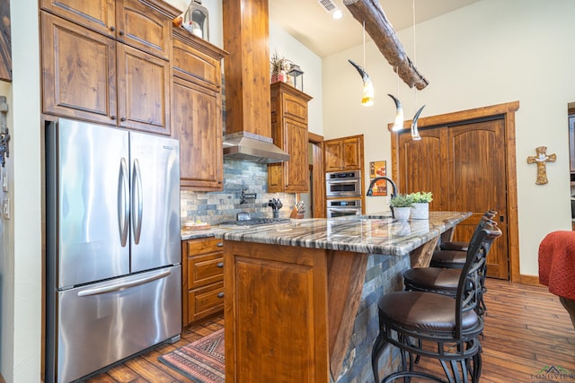 kitchen featuring tasteful backsplash, dark wood finished floors, a kitchen island with sink, stainless steel appliances, and a sink