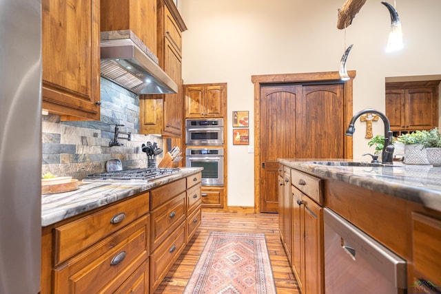 kitchen with light stone counters, light wood-style flooring, stainless steel appliances, a sink, and backsplash