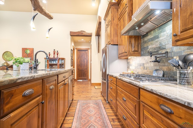 kitchen featuring stainless steel gas cooktop, brown cabinets, light stone counters, and exhaust hood