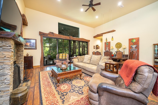 living room with a ceiling fan, visible vents, a stone fireplace, and hardwood / wood-style floors