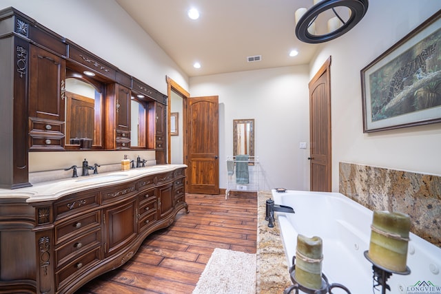 bathroom featuring a tub to relax in, recessed lighting, wood finished floors, visible vents, and double vanity