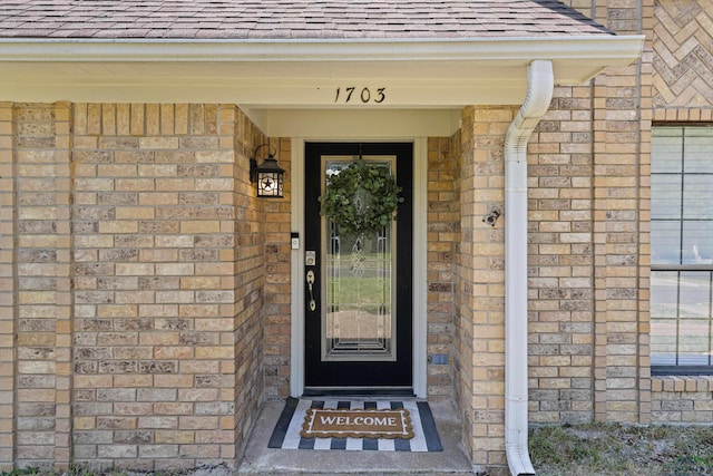 view of exterior entry featuring roof with shingles and brick siding